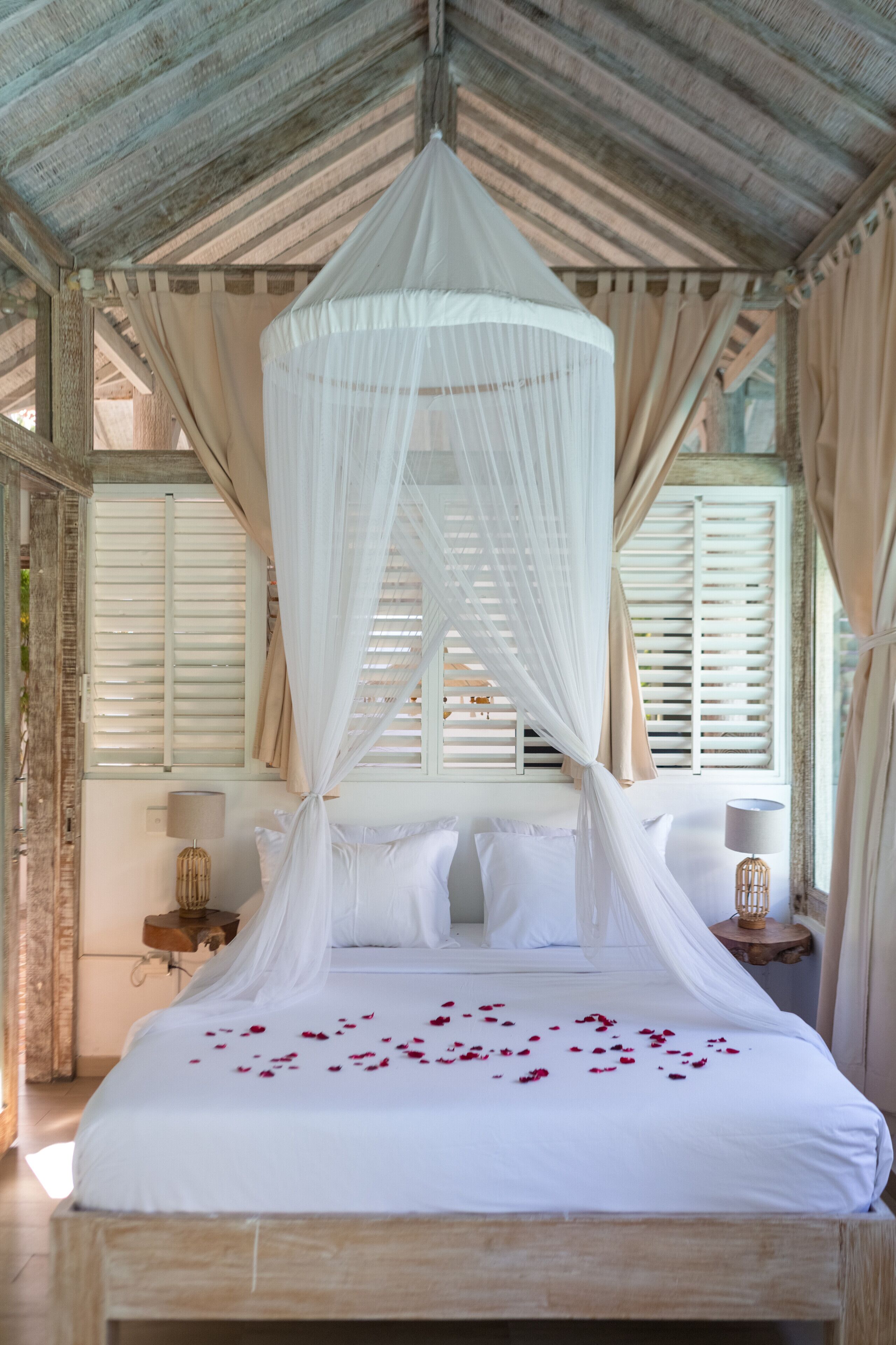 Una cama con dosel, ropa blanca de cama y pétalos de rosa.