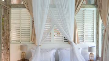 Una cama con dosel, ropa blanca de cama y pétalos de rosa.