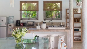 Une cuisine spacieuse avec une table à manger en verre, des chaises en bois, un ventilateur de plafond et une vue sur la verdure environnante.
