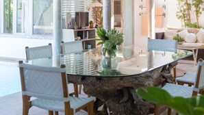 Un espace repas comprenant une table ronde en verre, des chaises en bois et un luminaire suspendu.