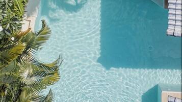 Vista aérea de una piscina con dos personas relajándose en el borde, rodeado de exuberante follaje.