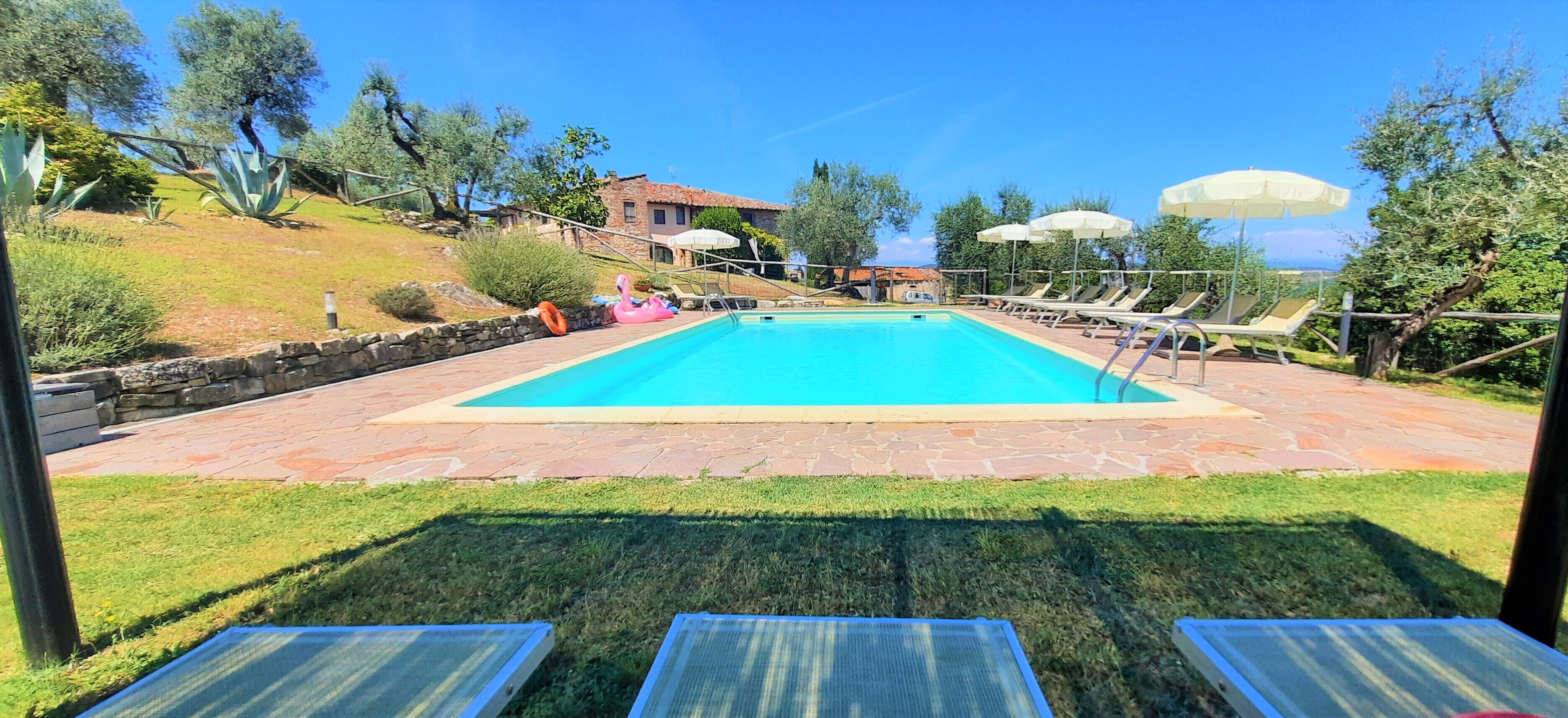 A rectangular swimming pool with a stone border, surrounded by a grassy area and a stone wall.