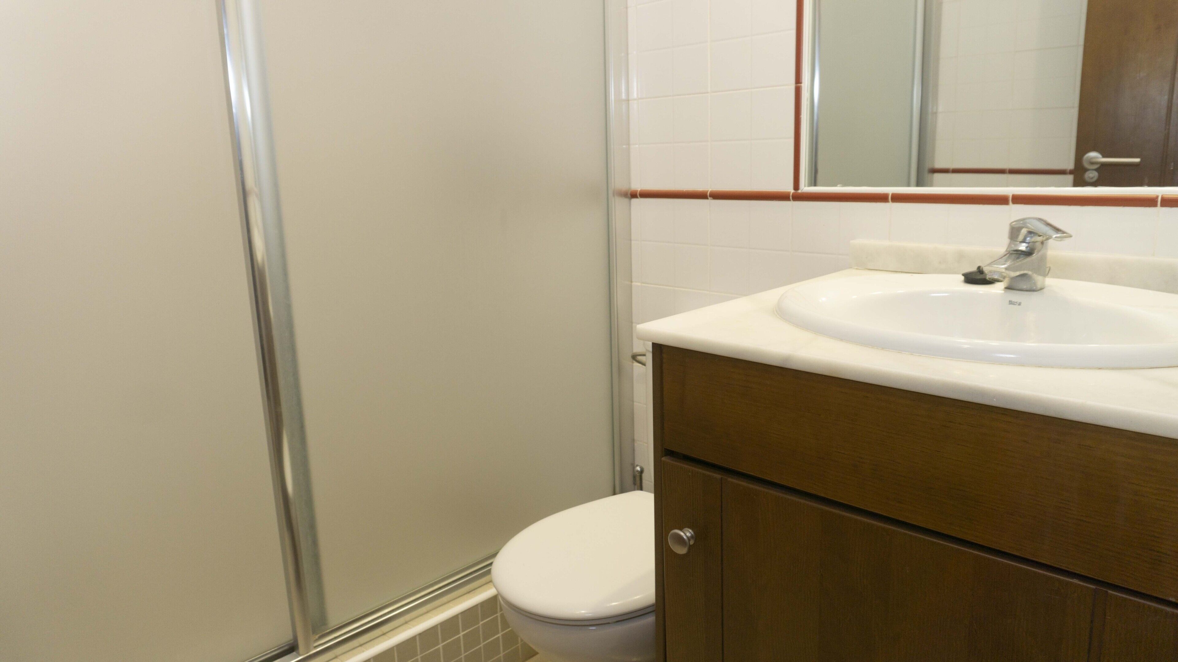 A bathroom with a white toilet, a white sink with a silver faucet, and a wooden cabinet.