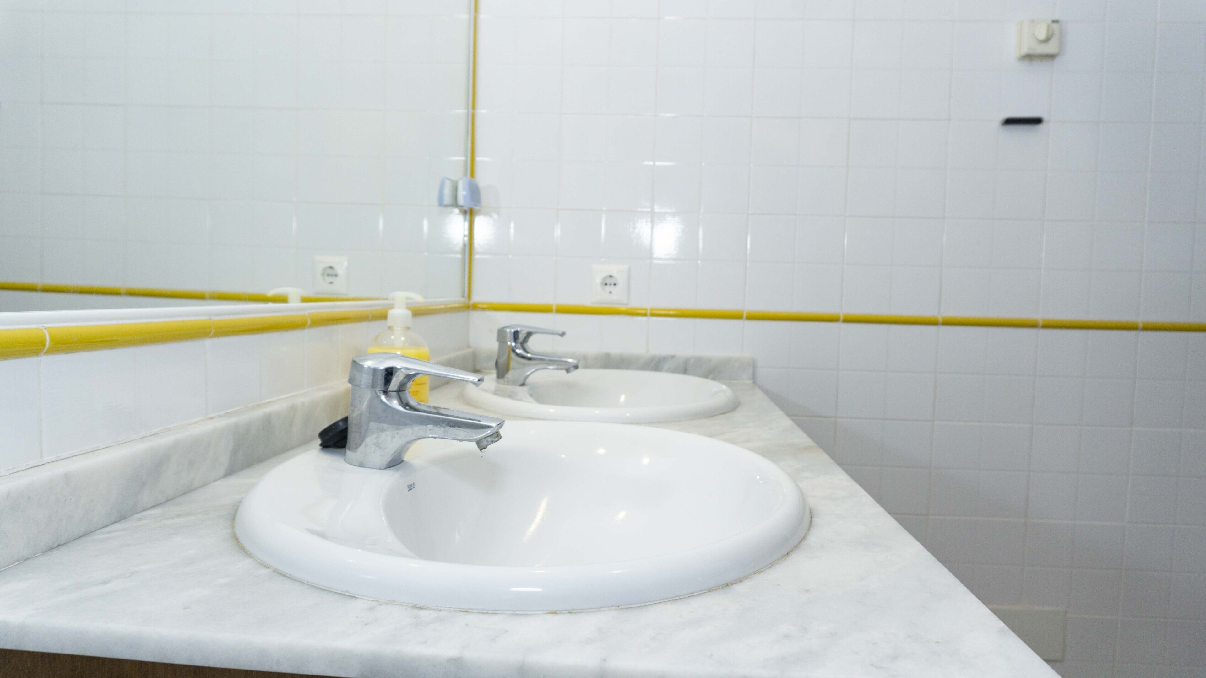 Un baño con dos lavamanos, un espejo y una franja amarilla en la pared.
