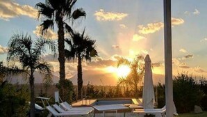 Ein überdachter Außenbereich mit Liegestühlen, einem Pool und Blick auf den Sonnenuntergang.