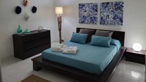Ein Schlafzimmer mit einem Bett, einer Kommode, einer Stehlampe und zwei an der Wand befestigten Bildern.