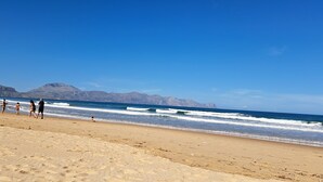 Ein Strand mit Menschen, die spazieren gehen und spielen, Berge im Hintergrund und klarem Himmel.