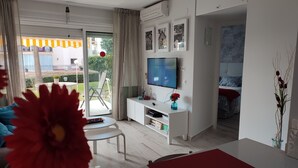 Una sala de estar moderna con un televisor de pantalla plana, un mueble blanco para entretenimiento y un ventanal corredero que da a un espacio exterior.