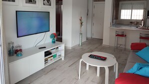 Una sala de estar moderna con un televisor de pantalla plana, un mueble blanco para equipo multimedia, una mesa de centro redonda y un sofá rojo.