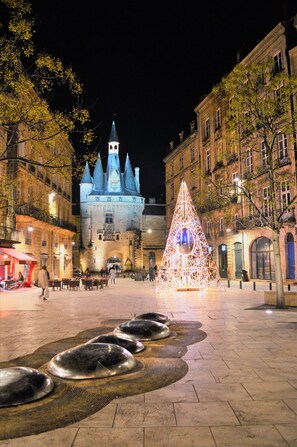 A courtyard with a large illuminated Christmas tree, a historic building with a tower, and a fountain with multiple basins.