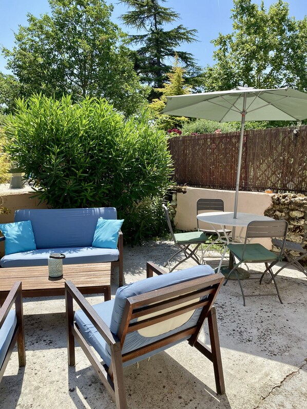 Un patio al aire libre con un sofá, sillas, una mesa y una sombrilla.