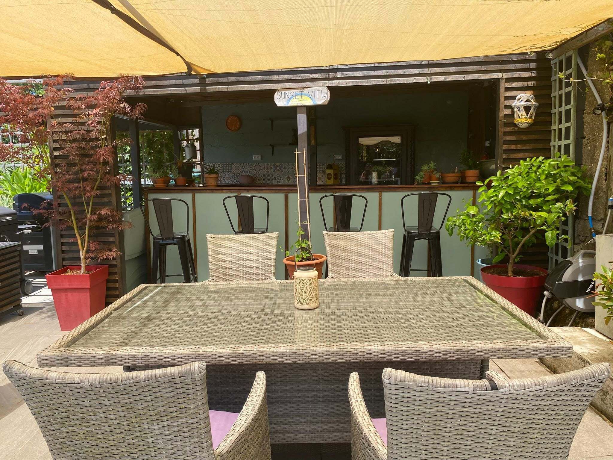Un espacio exterior para comer con una mesa y sillas, rodeado de plantas en macetas y una estructura de madera.