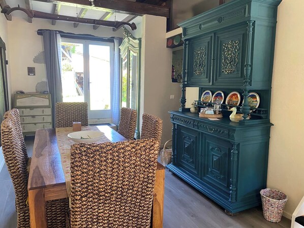 A dining area with a wooden table and woven chairs, a teal cabinet with decorative plates, and a view through a glass door.