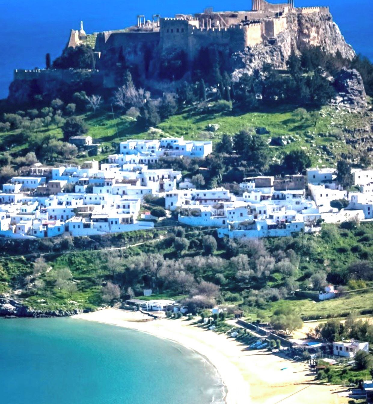 A coastal town with white buildings, a castle on a hill, and a beach.