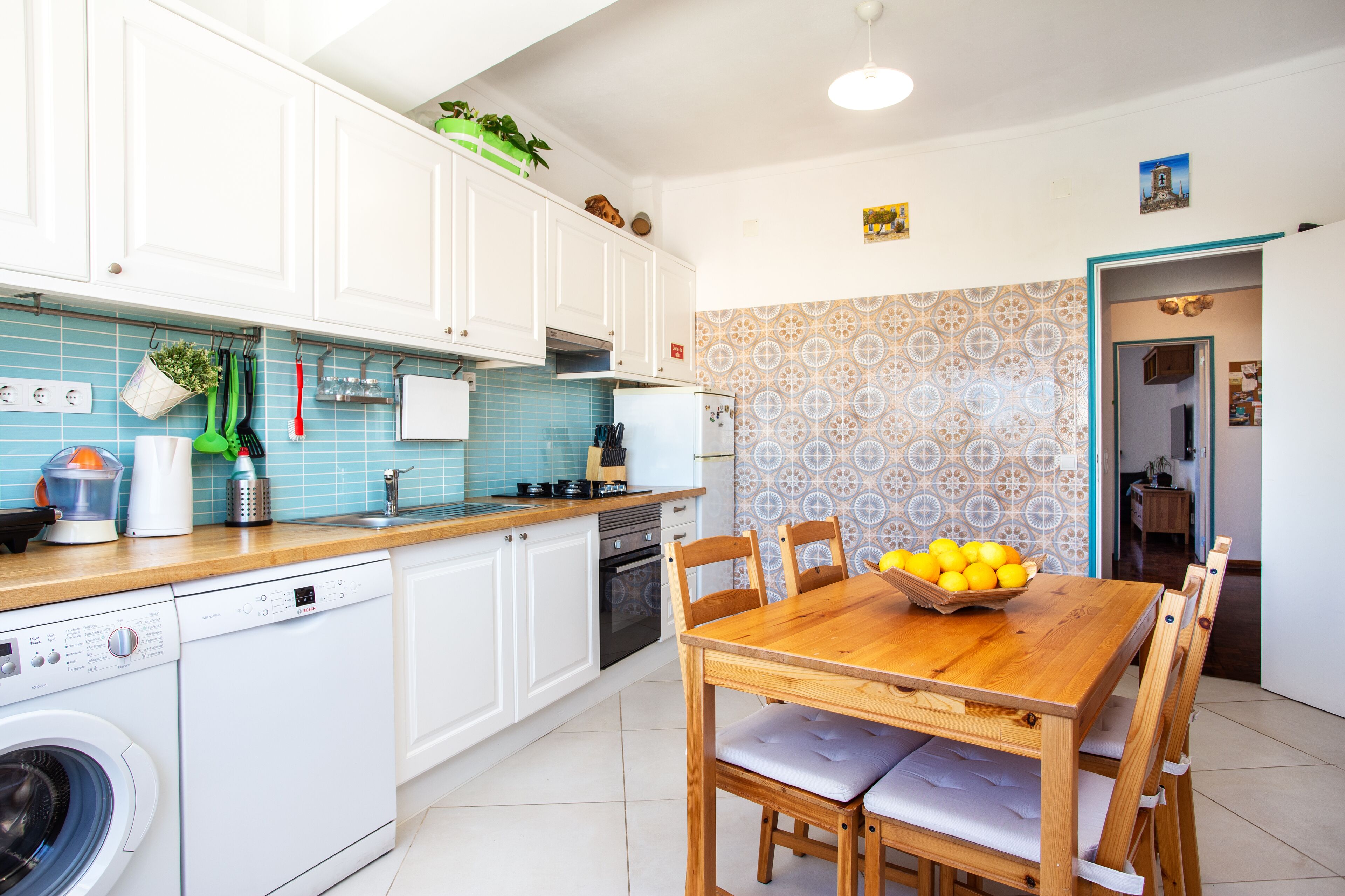 Een moderne keuken met witte kasten, een Bosch vaatwasser en een houten eettafel met een schaal fruit.