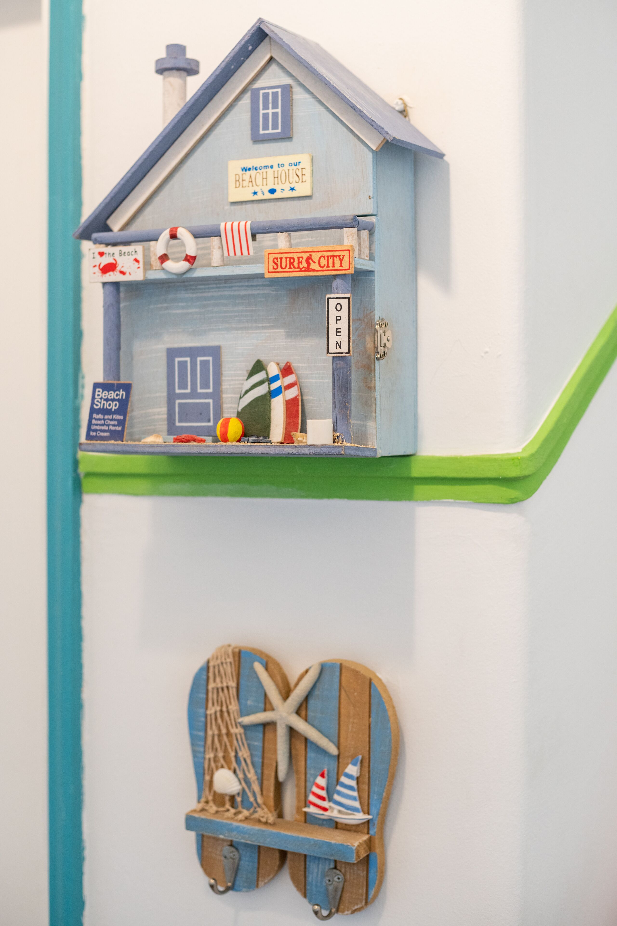 A beach-themed display with a house model, surfboards, and a beach shop sign.