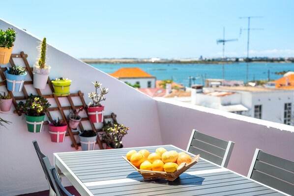 A balcony with a table and chairs, a basket of lemons, and potted plants.
