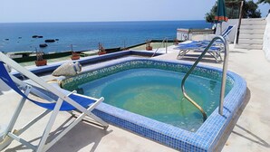 En swimmingpool med havudsigt, omgivet af liggestole og krukkeplanter.