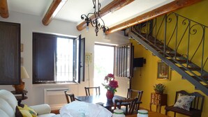 Un comedor con una mesa de madera, sillas, un jarrón con flores y una escalera con baranda de metal.