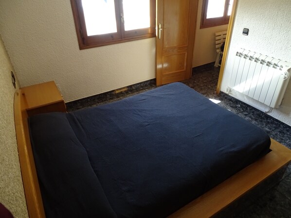 A room with a bed, a wooden nightstand, a radiator, and a window with wooden frames. - Gite in the Pyrenees (Guardiola de Berga)