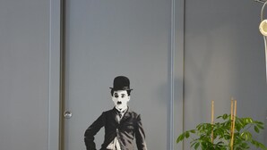 A door with a mural of a man in a suit and top hat, a potted plant, and a floor lamp. - Large apartment with 2 bedrooms and two bathrooms in PALAZZO SAN MATTEO (Palermo)