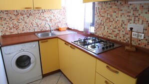 A compact kitchen with a washing machine, a sink, and a gas stove. - Casa Gabbiano B (Cefalù)