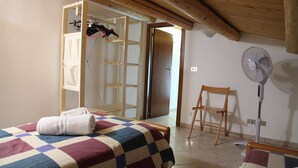 A bedroom with two beds, a wooden chair, a standing fan, and a door leading to another room. - Casa Gabbiano B (Cefalù)