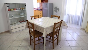 A dining area with a table covered by a checkered tablecloth, surrounded by wooden chairs. - Casa Gabbiano B (Cefalù)