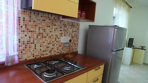 A kitchen with a gas stove, a refrigerator, and a tiled backsplash. - Casa Gabbiano B (Cefalù)
