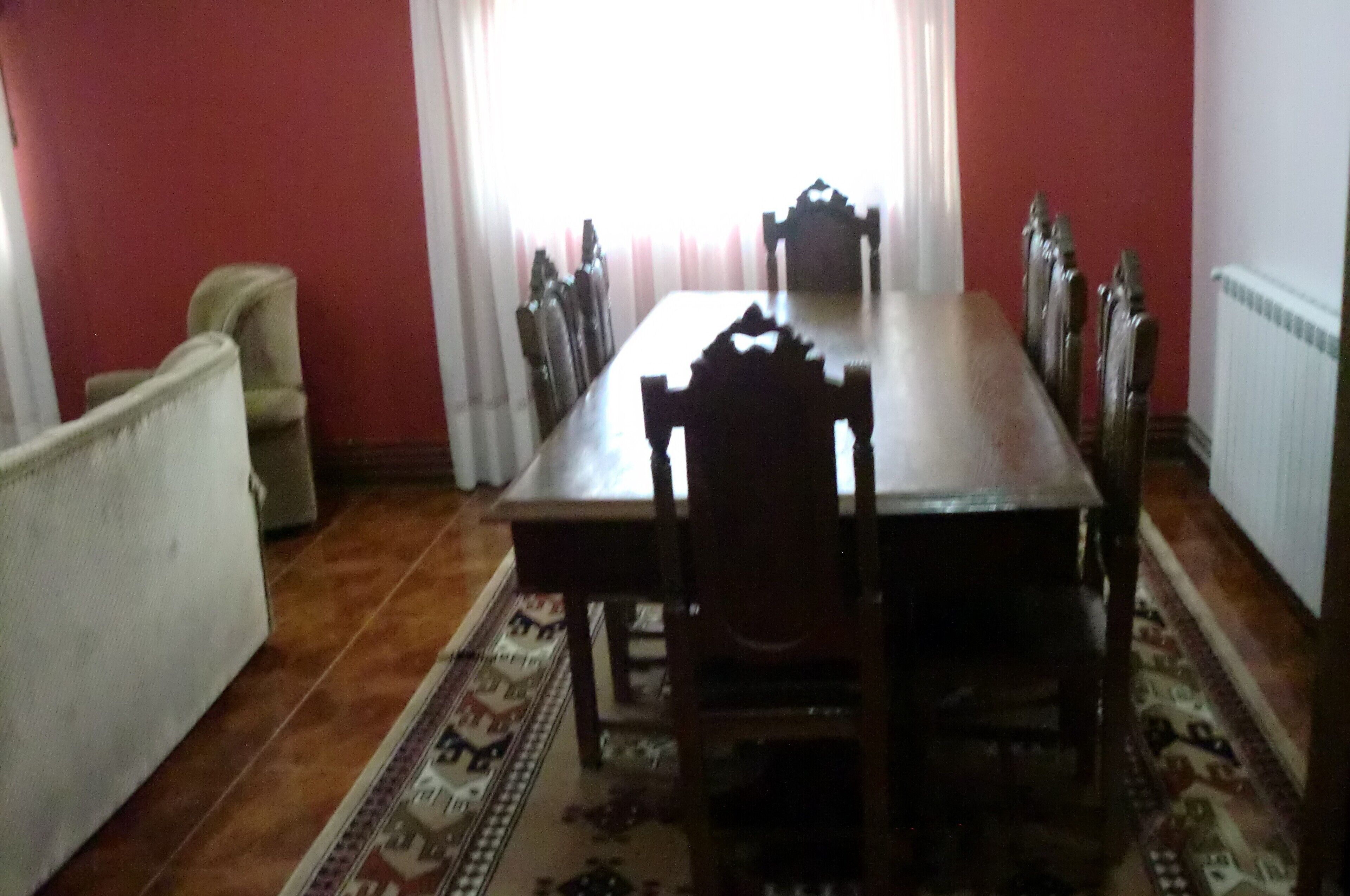 A dining area with a long wooden table and chairs, a patterned rug, and a radiator.