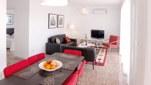 Een moderne woonkamer met een eethoek, een bank, een televisie en een rode fauteuil.