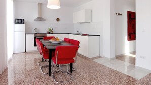 Een moderne keuken met witte kasten, een zwart aanrecht en een rode eettafel met stoelen.