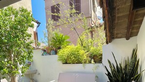 An outdoor patio with wooden flooring, white cushioned chairs, a small table, and potted plants.