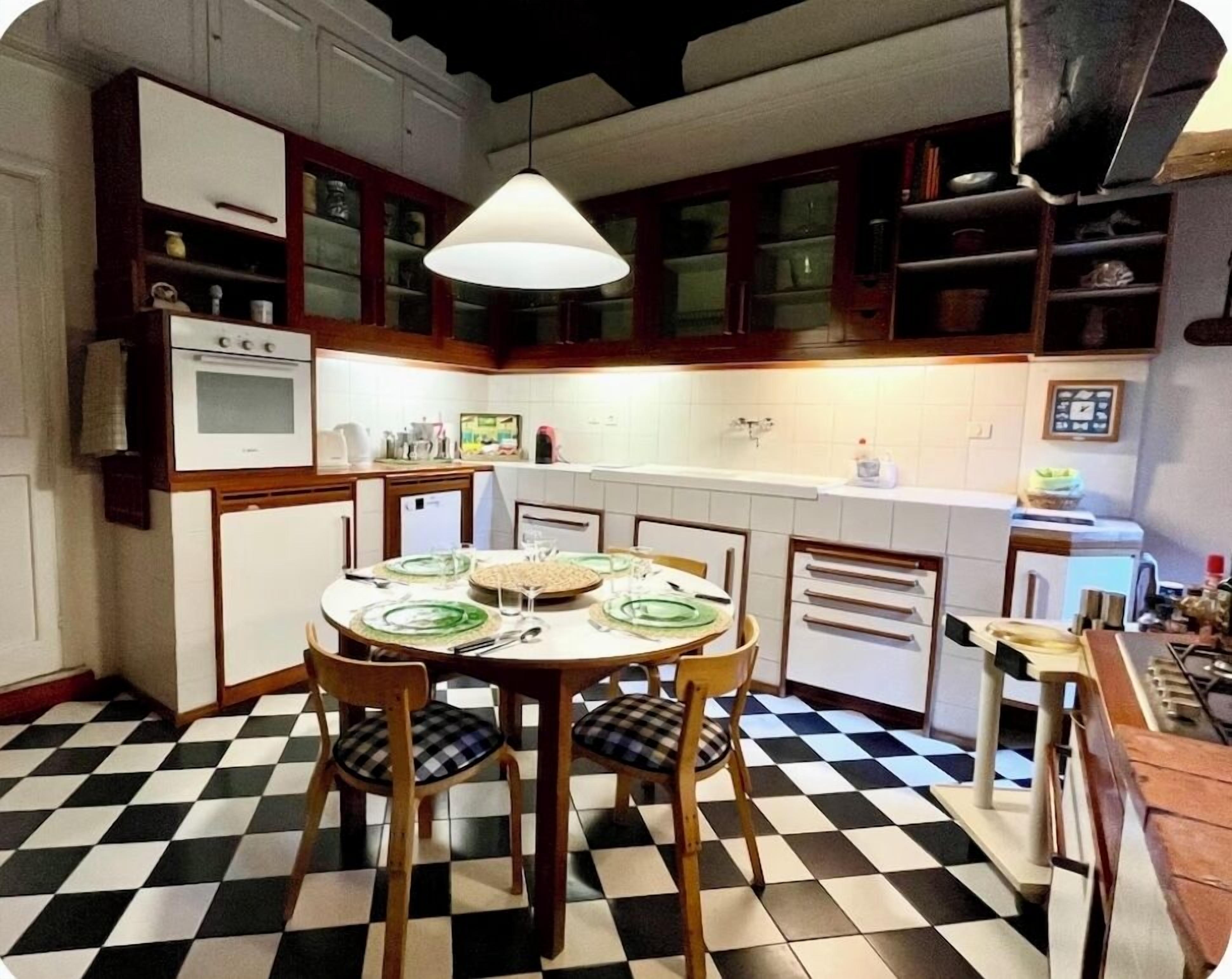 Una cocina con piso a cuadros, una mesa redonda con sillas y una lámpara colgante.