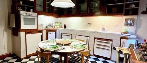Una cocina con piso a cuadros, una mesa redonda con sillas y una lámpara colgante.