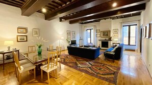 A spacious living room with wooden flooring, a blue sofa, a dining area with a glass table, and a fireplace.