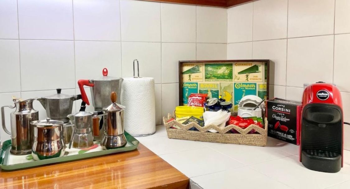Una cocina con cafetera, jarra de café, hervidor, tetera y una cesta de cápsulas de café, además de una caja de cápsulas.