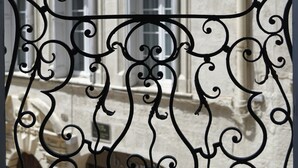 Een balkon met gedetailleerd zwart metalen hekwerk en een gebouw met ramen met witte kozijnen op de achtergrond.