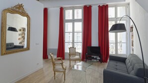 Een woonkamer met een bank, twee stoelen, een televisie en een grote spiegel.