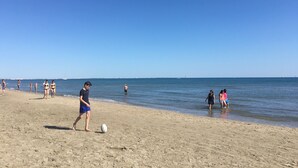 Een zandstrand met mensen die spelen en wandelen in de buurt van het water.