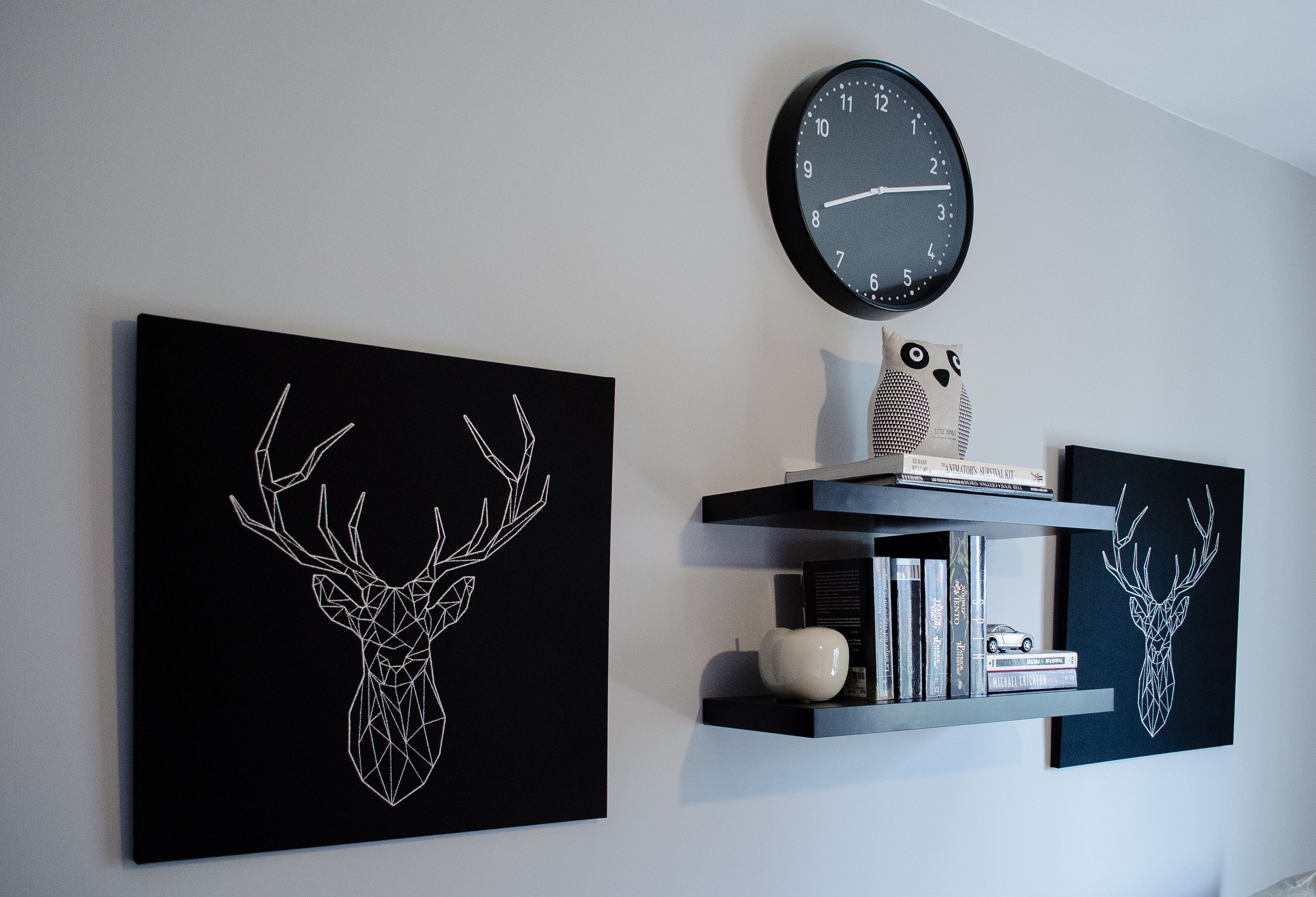 A wall with two framed deer head artworks, a clock, and a shelf with books and decorative items.