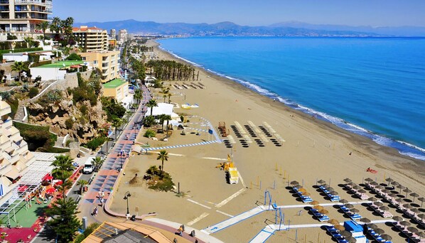 Paisagem costeira com praia, edifícios de hotel e mar azul cristalino.