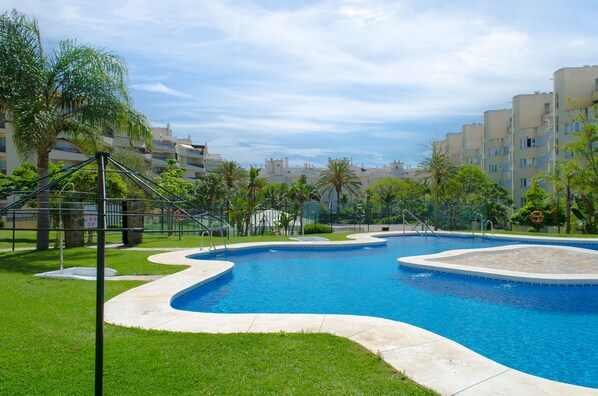 A swimming pool with a curved design, surrounded by a grassy area and palm trees.