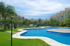 Piscina com design curvo, cercada por gramado e palmeiras.