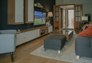 Uma sala de estar moderna com uma televisão de tela plana, uma mesa de centro de vidro e dois sofás.