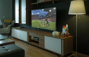 Uma sala de estar moderna com uma grande TV de tela plana fixada em um móvel de madeira, um sofá confortável, uma pequena mesa de centro e um abajur.