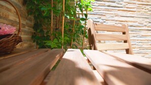 A wooden table and chair set against a stone wall with green foliage.