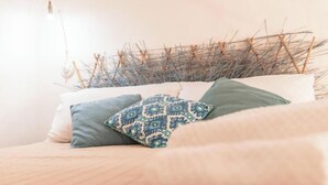 A bed with a woven headboard, a white pillow, a blue pillow, and a patterned pillow.