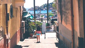 A narrow alleyway with a person walking towards a coastal area with buildings and a view of the sea.