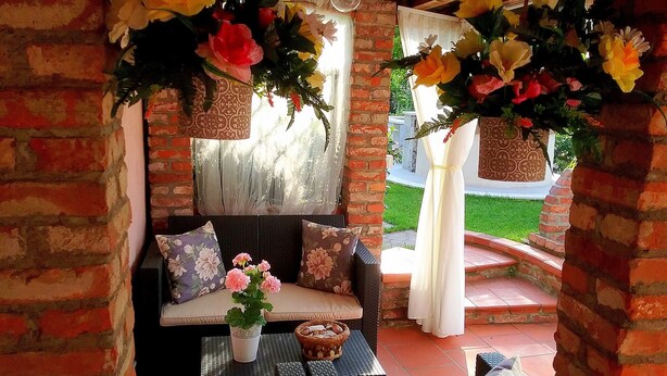 A cozy outdoor seating area with a brick wall, a cushioned bench, and a table with a potted plant. - Amaryllis vacation homes - pink house - CODE CIN: IT011002B4COYDJRPS (Romito Magra)